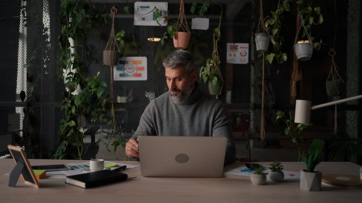 Middle-Aged Man Working On Laptop In Modern Office With Plants