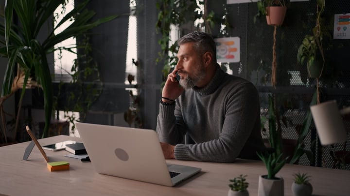 Bearded Man Focused While Talking On Phone In Modern Biophilic Office