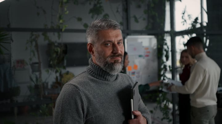 Middle-Aged Man In Turtleneck Holding Tablet In Modern Office