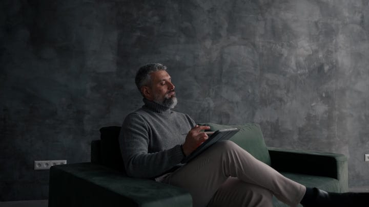 Mature Man Relaxing On Couch While Interacting With Tablet