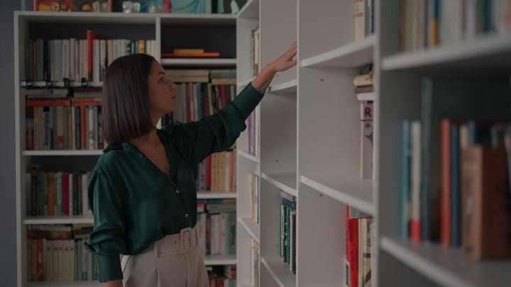 Businesswoman Searches For Inspiration Among Office Bookshelves