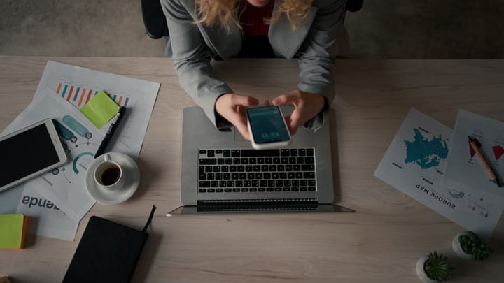 Overhead View Of Businesswoman Using Smartphone While Working At Office Desk
