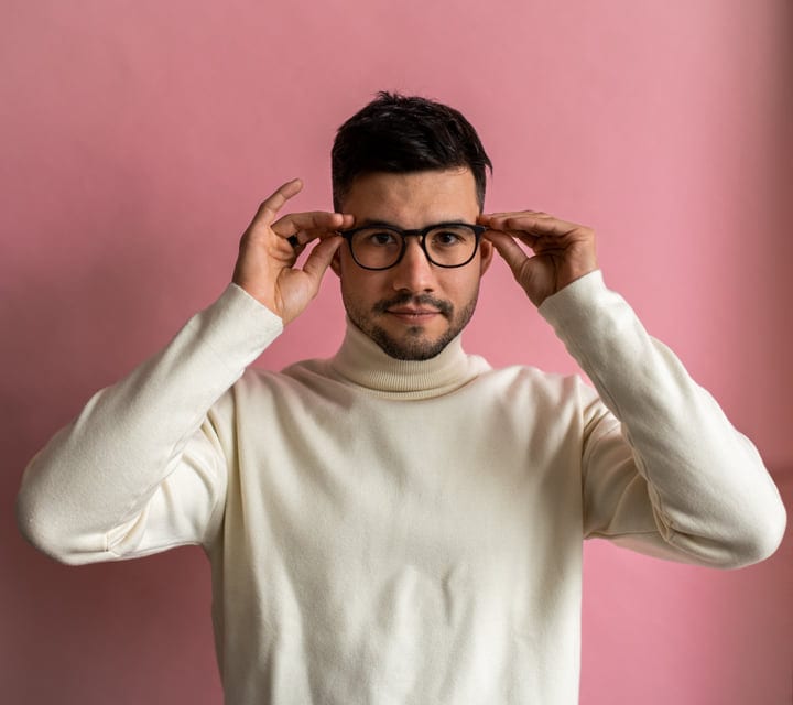 Confident Young Professional Adjusts Glasses Against Pink Background