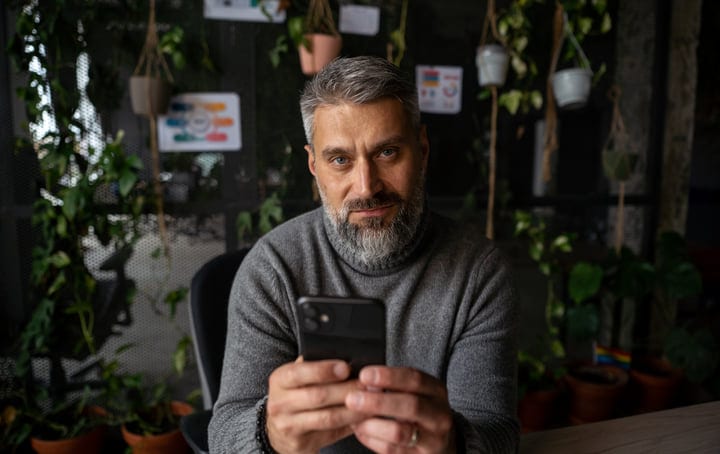 Bearded Man Engages with Smartphone in Lush Office Space
