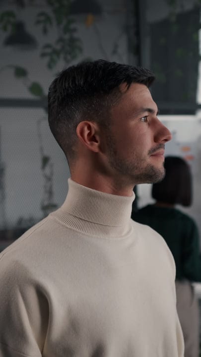 Young Man In Turtleneck Sweater Looking Thoughtfully In Modern Office