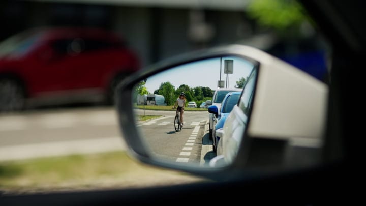 Cyclist Approaches In The Car's Side Mirror Reflection