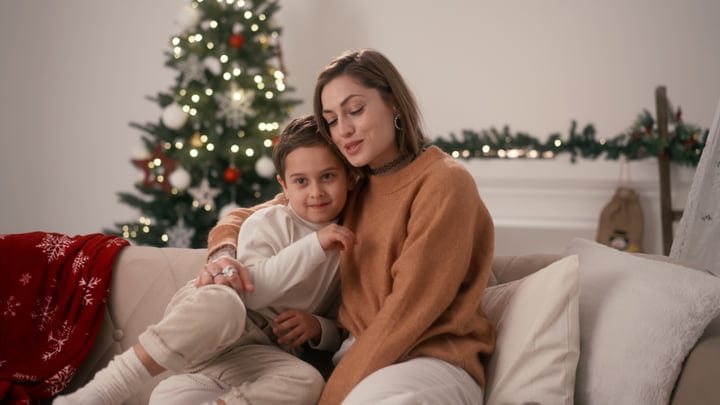 Mother And Child Cuddle By The Christmas Tree