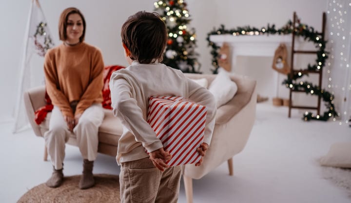 Young Child Surprises Mother With Christmas Gift In Living Room