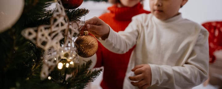 Young Hands Carefully Place Bauble on Christmas Tree