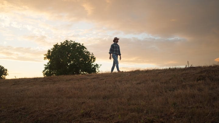 A Farmer Walks Silhouetted Against a Glowing Sunset