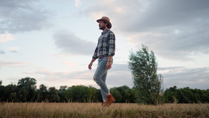 Reflective Farmer Strolls Through A Golden Field At Dusk