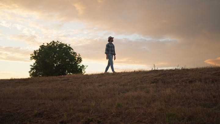 A Farmer Walks Thoughtfully Under A Golden Sunset Sky