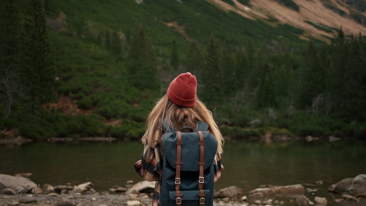 Exploring Tranquil Wilderness In A Red Beanie And Backpack