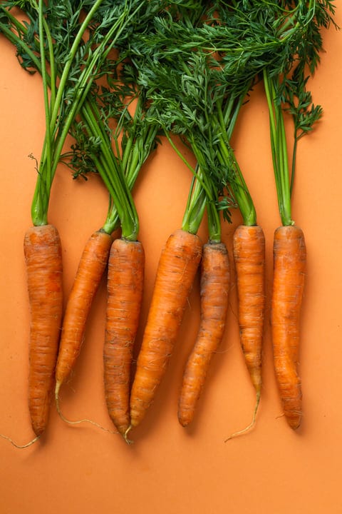 Vibrant Carrot Bunches Against A Warm Orange Canvas