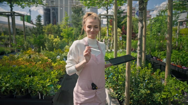 Young Gardener Smiles While Pruning in Lush Greenhouse