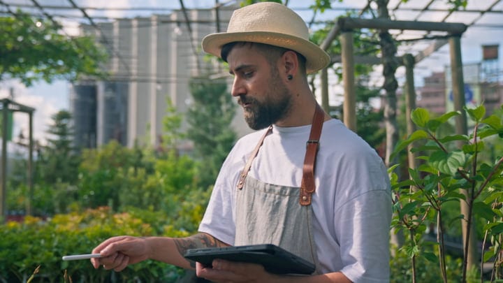 Modern Gardener Uses Tablet Among Lush Greenhouse Foliage