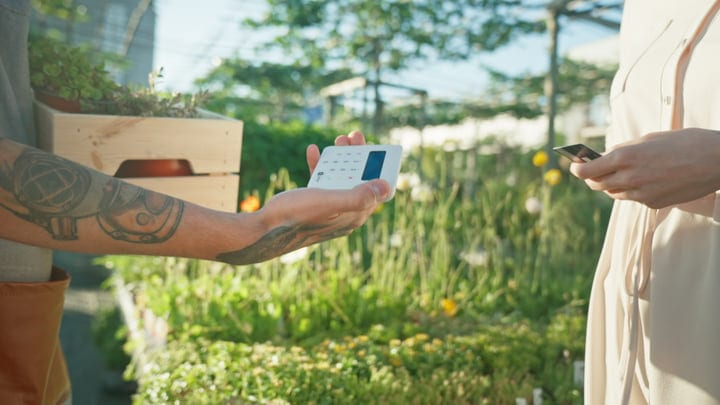 Tattooed Gardener Processes Payment in Lush Greenhouse