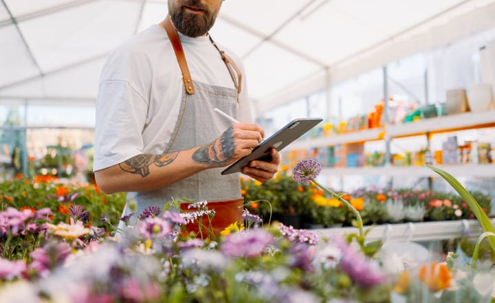 Tattooed Gardener Recording Data in Blooming Greenhouse
