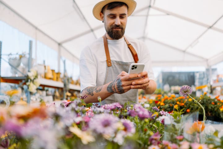 A Gardener Checks His Phone Amidst Blooming Flowers