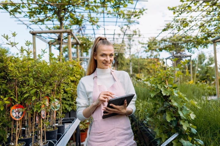 Smiling Gardener Checks Tablet in Lush Greenhouse