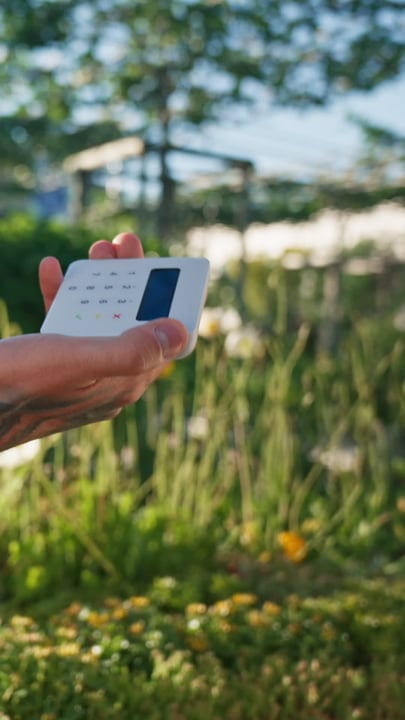 Hands Holding Payment Device in Sunlit Garden