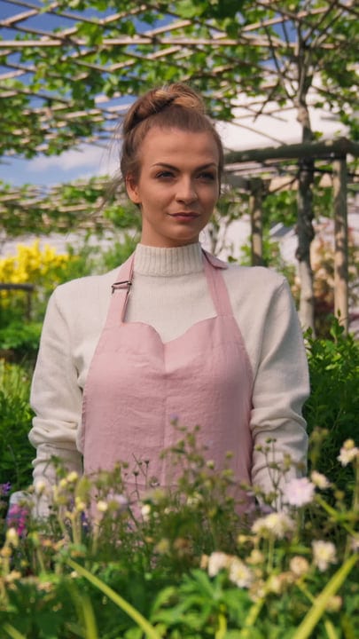 Serene Gardener Tending Flowers In A Lush Greenhouse