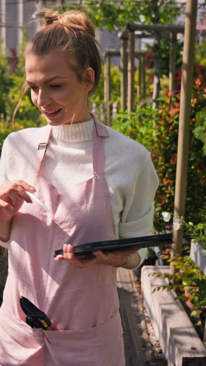 Gardener Checks Notes While Pruning in Greenhouse