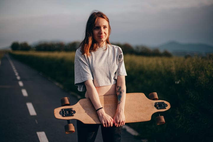 Young Woman Embraces Her Skateboard On Country Road