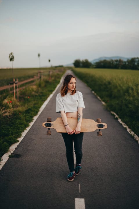 Young Skateboarder Ponders Her Path On Country Road
