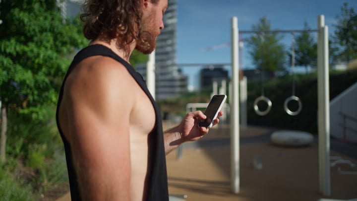 Urban Athlete Checks Smartphone In Outdoor Gym