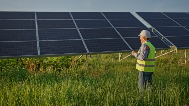 Engineer Evaluates Solar Panels in Lush Green Field