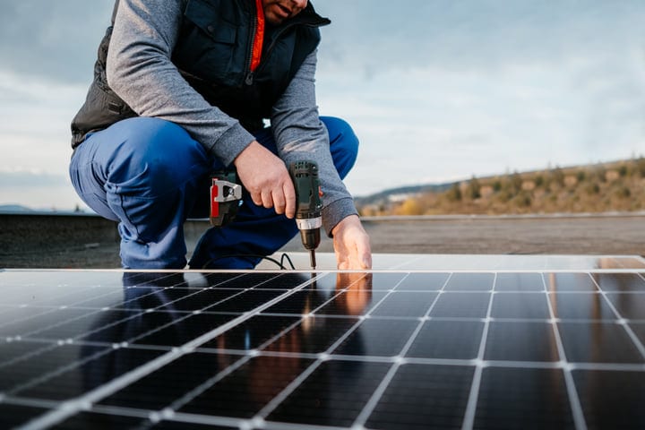 Solar Technician Secures Panels on a Rooftop Under Clear Skies