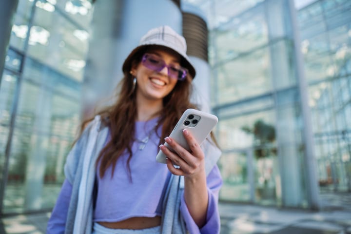 Smiling Young Woman Engages With Her Smartphone Outdoors