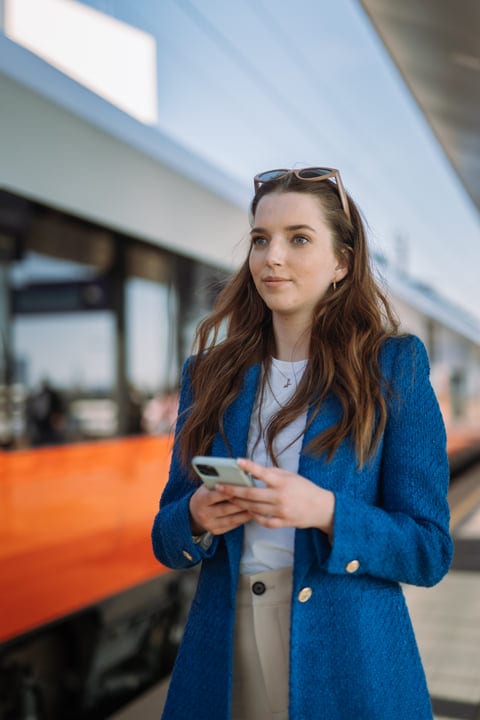 Young Woman Awaits Train While Checking Her Phone
