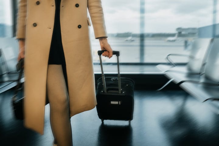 Traveler in Beige Coat Navigates Busy Airport Terminal