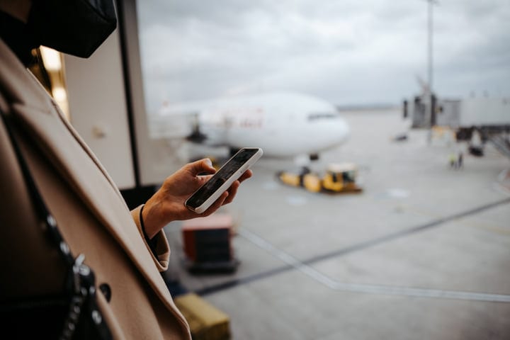 Traveler Engages With Smartphone In Busy Airport Terminal