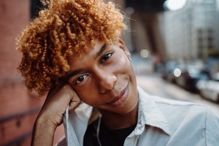 Curly-Haired Youth Smiling Brightly On A Busy NYC Street