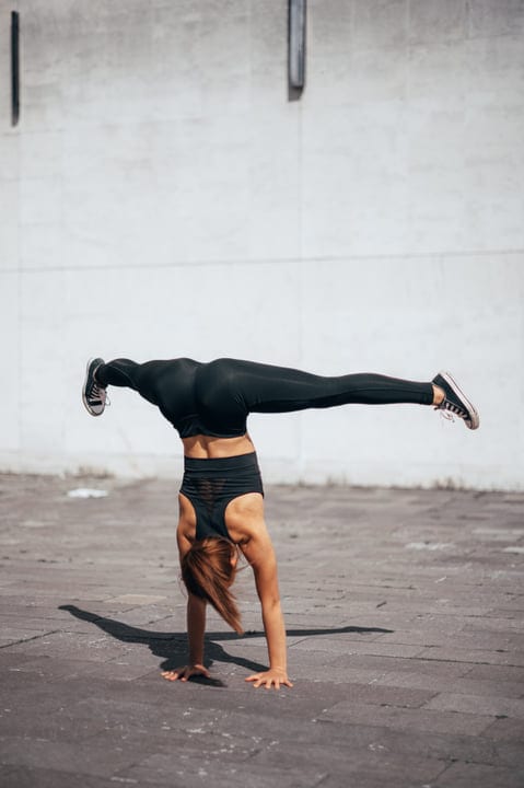 Fearless Woman Handstands In Urban Landscape Under Sunlight