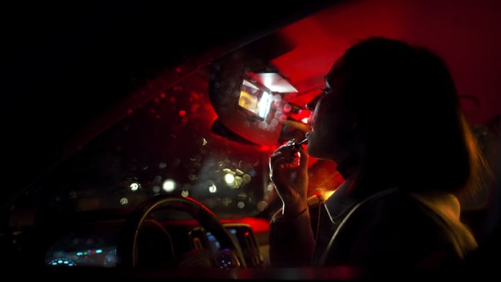 Red Lights Reflect Off Businesswoman Applying Lipstick At Night