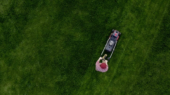 A Gardener Skillfully Maneuvers Mower Across Lush Lawn