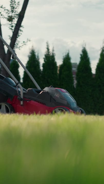 Close-Up Of Red Lawn Mower In Lush Green Garden