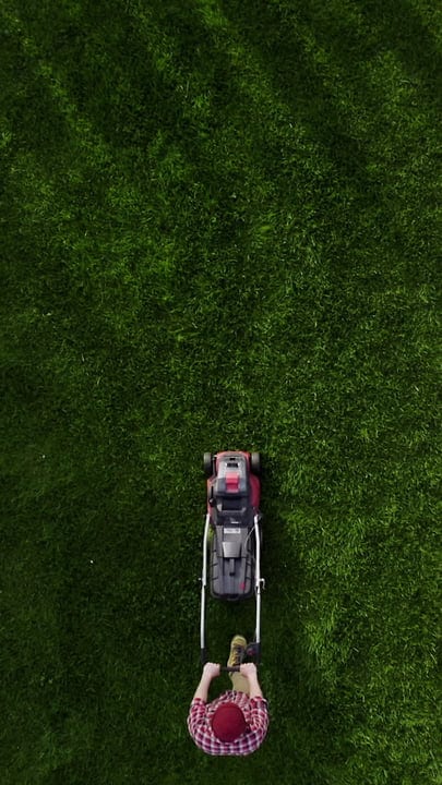 Top-Down View Of Gardener Mowing Lush Green Lawn
