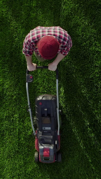Gardener in Plaid Shirt Mowing a Lush Green Lawn