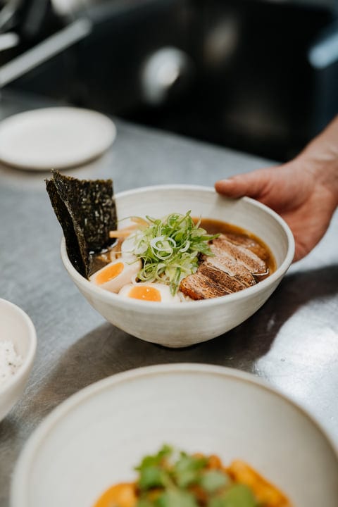 A Hand Presents Gourmet Ramen Bowl with Elegance