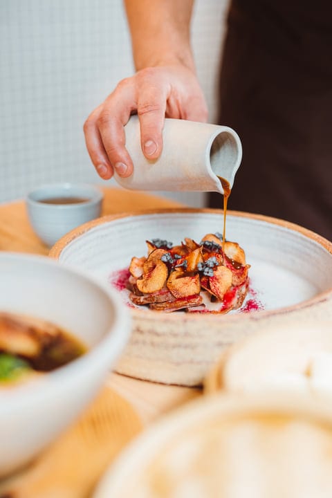 A Hand Pours Rich Sauce Over Gourmet Dish