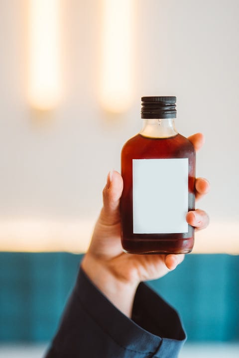 Hand Holding Syrup Bottle in Warm Indoor Light
