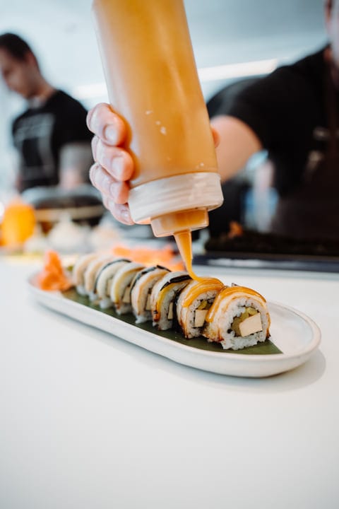 A Chef's Hand Finishes Sushi With Vibrant Sauce