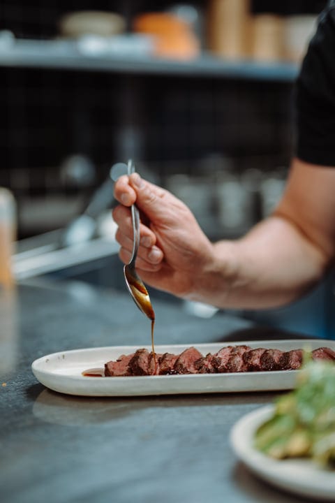 Artisan Hand Drizzling Sauce Over Gourmet Beef