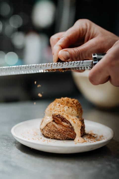 A Chef's Hand Perfecting A Dessert With Nutmeg Dust