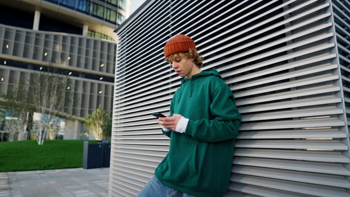 Young Man In Green Hoodie And Orange Beanie Checking Phone Outdoors